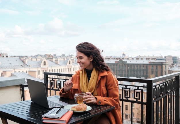 Junge Frau sitzt am Tisch mit Laptop und trinkt Tee im Café im Freien