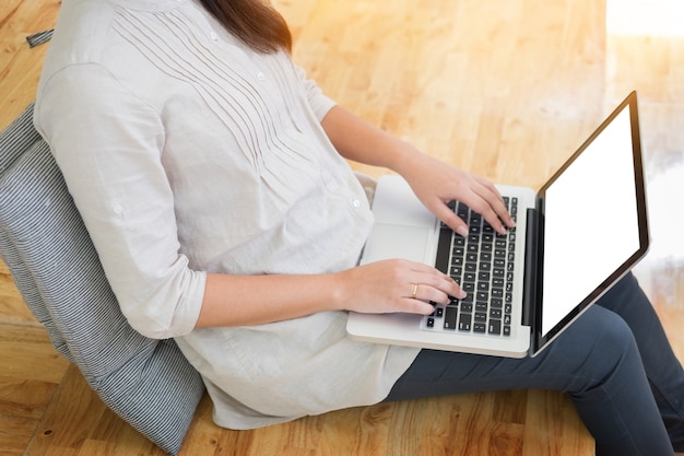 Junge Frau sitzt auf dem Boden mit Laptop in Bibliothek, Bildung und Technologie-Konzept.