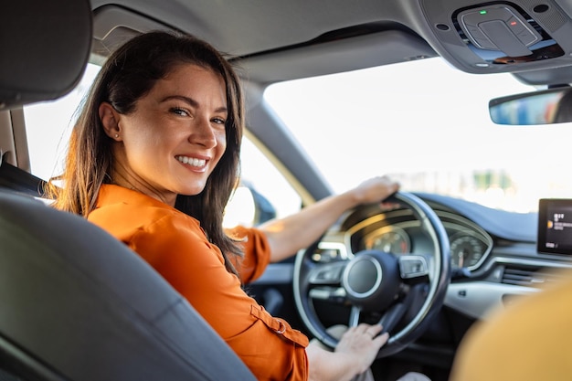 Junge Frau sitzt auf dem Fahrersitz im Auto und blickt über die Schulter in die Kamera. Porträt einer angenehmen Frau mit positivem Gesichtsausdruck, die mit einer unvergesslichen Autofahrt zufrieden ist