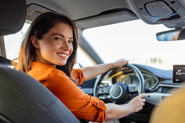 Junge Frau sitzt auf dem Fahrersitz im Auto und blickt über die Schulter in die Kamera. Porträt einer angenehmen Frau mit positivem Gesichtsausdruck, die mit einer unvergesslichen Autofahrt zufrieden ist