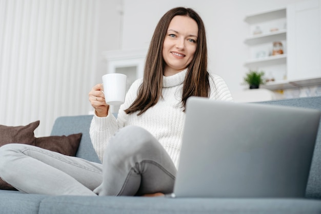 Junge Frau sitzt auf der Couch und benutzt einen Laptop