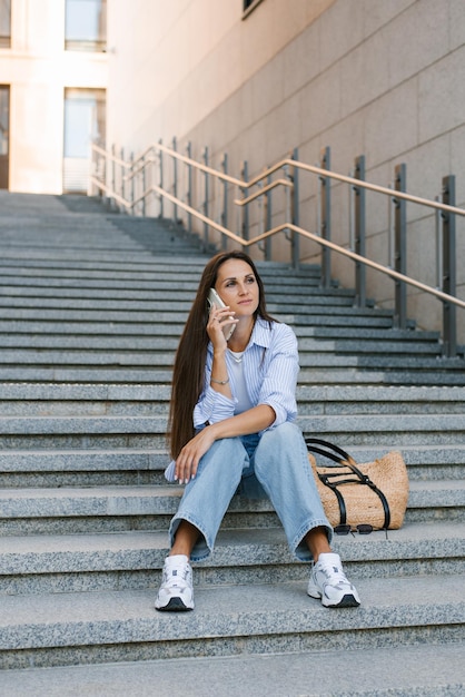 Foto junge frau sitzt auf der treppe und spricht mit ihrem handy