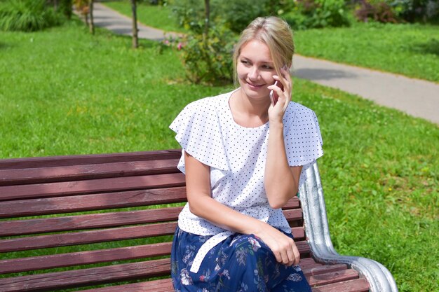 junge Frau sitzt auf einer Bank im Park mit Handy und spricht online