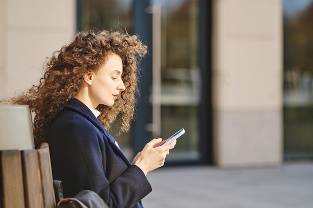 Junge Frau sitzt auf einer Bank und scrollt durch das soziale Netzwerk