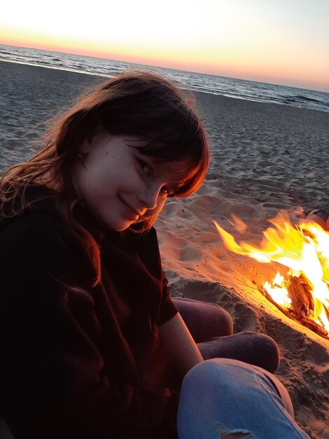 Foto junge frau sitzt bei sonnenuntergang am strand gegen den himmel