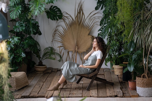 Junge Frau sitzt entspannt auf einem bequemen Sessel im stilvollen Innengarten mit grünen exotischen Pflanzen