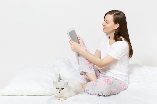 Junge Frau sitzt im Bett mit weißer süßer persischer silberner Chinchilla-Katze isoliert auf weißer Wand