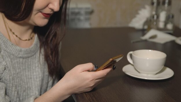 Junge Frau sitzt im Café mit Telefon und trinkt Tee, Nahaufnahme