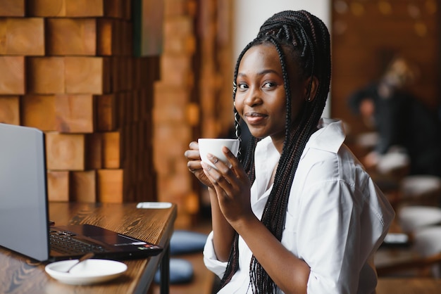 Junge Frau sitzt im Café, trinkt Kaffee und arbeitet am Laptop