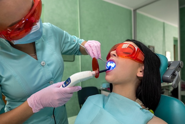 Junge Frau sitzt im Zahnarztstuhl und macht Bleaching-Verfahren unter der Kontrolle des Arztes