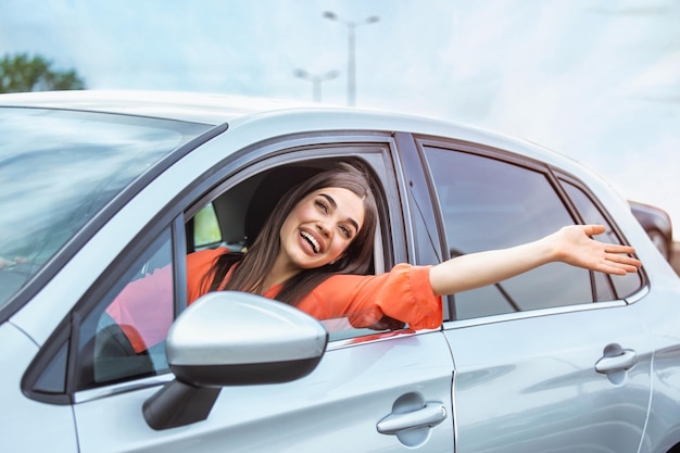 Junge Frau sitzt in einem Auto mit der Hand aus dem Fenster Glückliche Frau fährt ein Auto und lächelt Porträt einer glücklichen Fahrerin, die ein Auto mit Sicherheitsgurt steuert