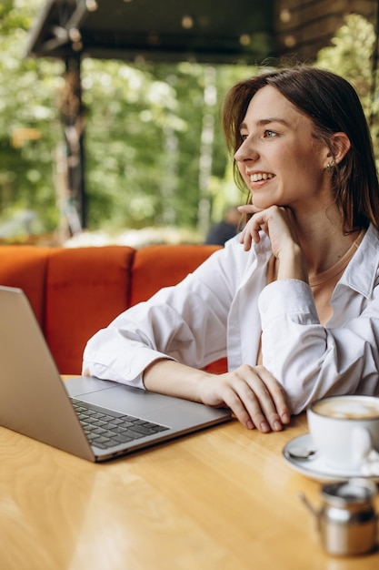 Junge Frau sitzt in einem Café, trinkt Kaffee und arbeitet am Computer