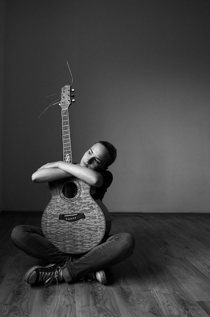 Foto junge frau sitzt mit gitarre auf dem holzboden zu hause