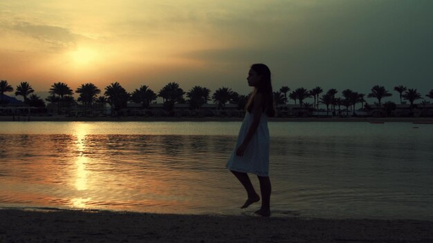 Junge Frau spaziert am Strand. Barfüßiges Mädchen verbringt die Zeit des Sonnenaufgangs am Meer