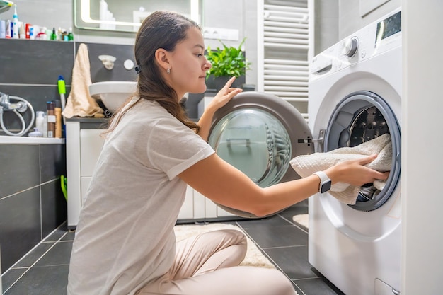 Junge Frau steckt Kleidung in die Waschmaschine im Badezimmer des Hauses ein
