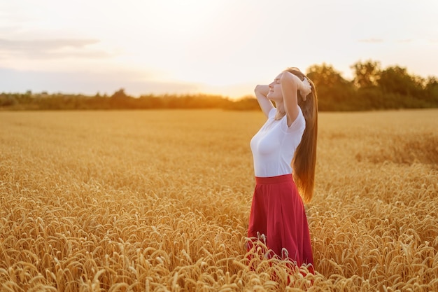 Junge Frau steht mitten im Bereich des reifen Weizens bei Sonnenuntergang Natürliche Schönheit
