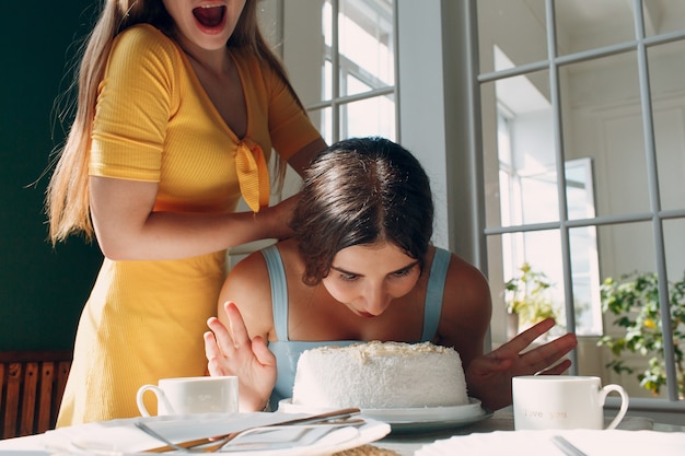 Junge Frau taucht Gesicht in weißen Kuchen mit Sahne. Alles Gute zum Geburtstag Konzept.