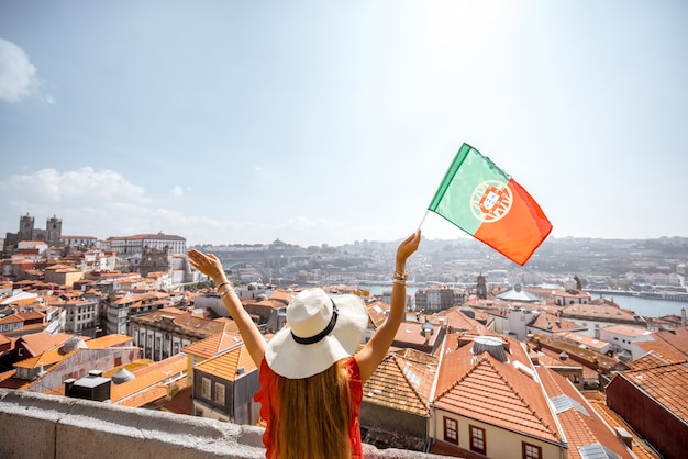 Junge Frau Tourist im roten Kleid mit portugiesischer Flagge auf dem Hintergrund der Altstadt Reisen in Porto, Portugal?