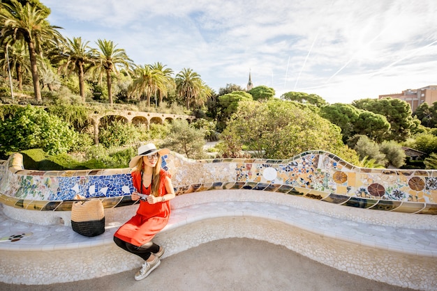 Junge Frau Tourist im roten Kleid sitzt auf der mit Mosaik verzierten Bank im berühmten Park Güell in Barcelona. Weitwinkelbild mit Kopierraum