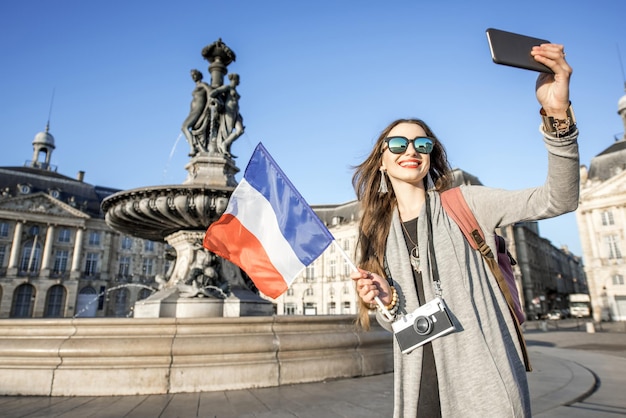 Junge Frau Tourist macht Selfie-Foto mit französischer Flagge auf dem berühmten Platz de la Bourse in der Stadt Bordeaux