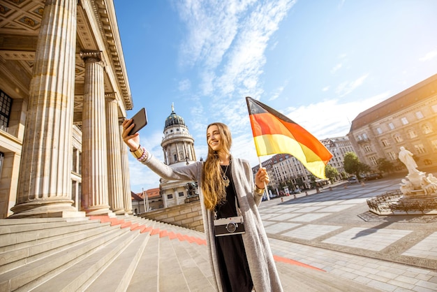 Junge Frau Tourist macht Selfie-Foto stehend mit deutscher Flagge auf der Treppe in der Nähe des Konzerthauses in Berlin