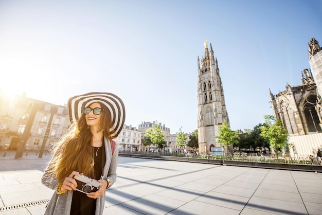 Junge Frau Tourist mit Fotokamera auf dem Platz Pey-Berland mit Glockenturm im Hintergrund während des Morgens in Bordeaux Stadt spazieren