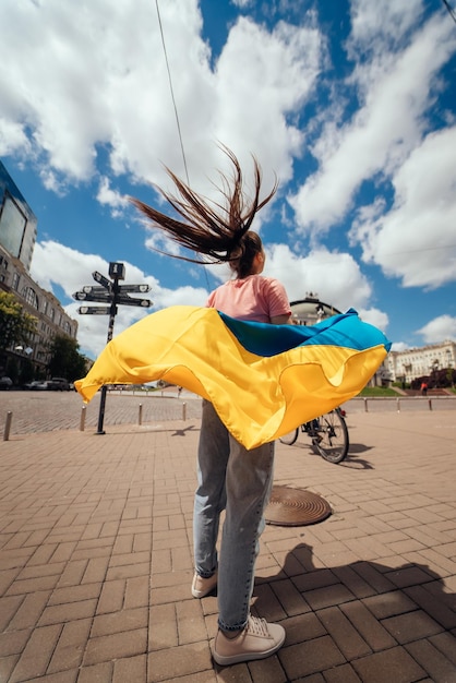 Junge Frau trägt die Flagge der Ukraine, die hinter ihr flattert