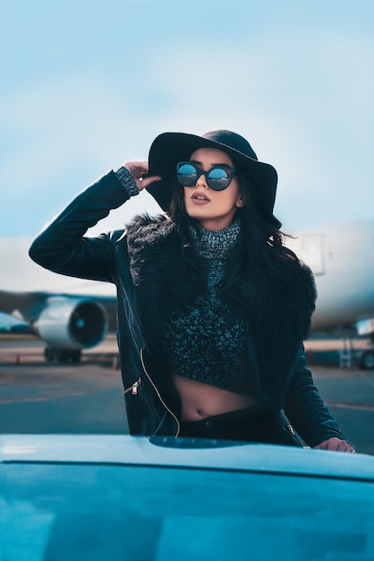 Junge Frau trägt eine Sonnenbrille gegen ein Flugzeug in einem Fahrzeug auf der Landebahn