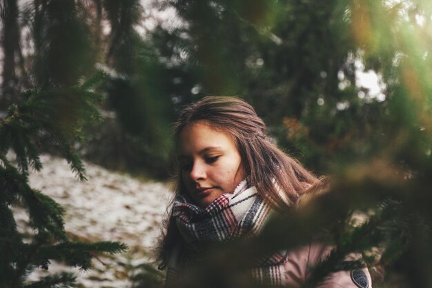 Foto junge frau trägt einen schal, während sie gegen bäume steht