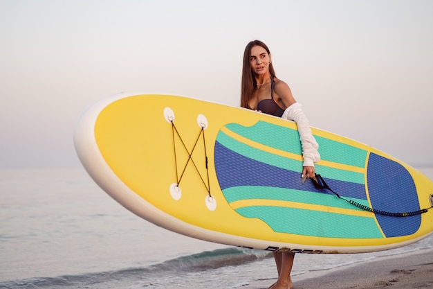 Junge Frau trägt Paddle Board am Strand