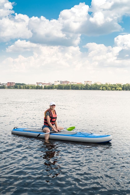 Junge Frau trägt Schwimmweste, Paddle-Boarding auf einem schönen See am heißen Sommertag, aktiver Lifestyle-Sport und Entspannung