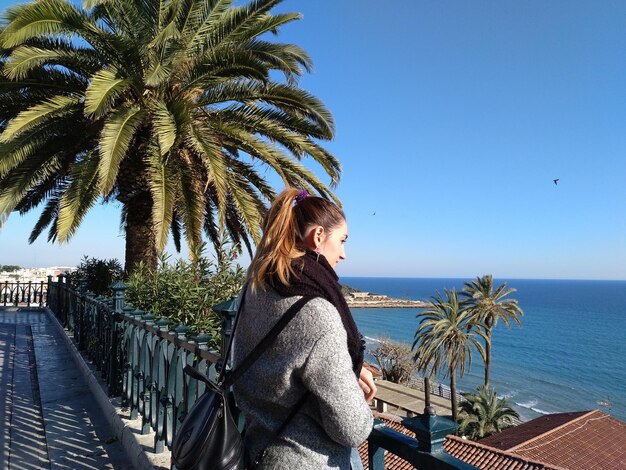 Foto junge frau trägt warme kleidung, während sie auf das meer schaut