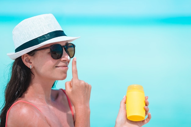 Junge Frau tragen Creme auf ihre Nase am Strand auf