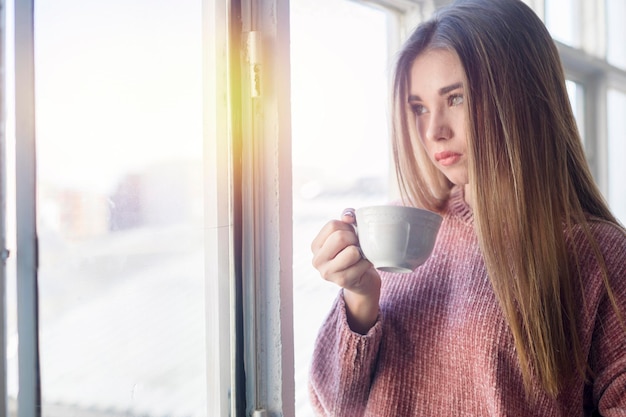 Junge Frau trinkt Kaffee am Fenster zu Hause