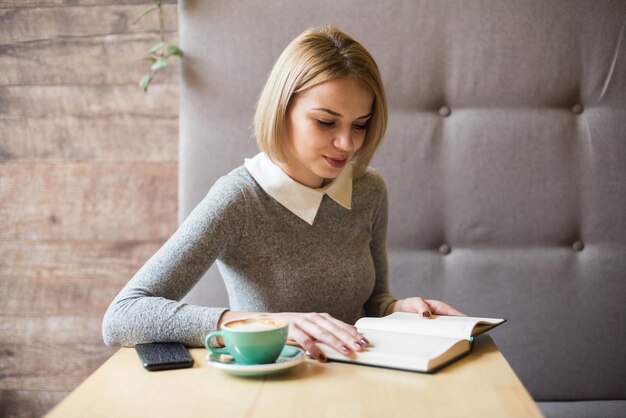 Foto junge frau trinkt kaffee im café und liest ihre molkerei sie sitzt am tisch