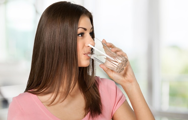 Junge Frau trinkt Wasser aus Glas, auf unscharfem Hintergrund