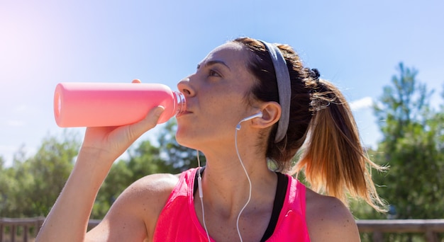 Junge Frau trinkt Wasser, nachdem sie mit Kopfhörern Musik gehört hat Gesunder Lebensstil