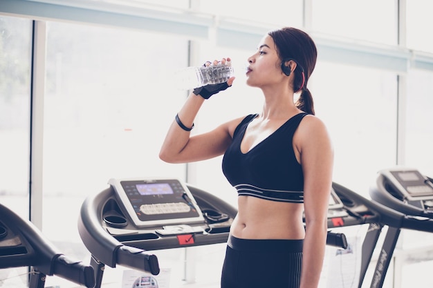 Junge Frau trinkt Wasser, während sie im Fitnessstudio steht