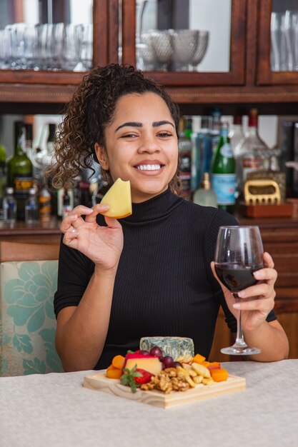 Junge Frau trinkt Wein und isst Käse allein im Wohnzimmer. Frau, die Käsesnacks isst und Wein trinkt, um sich nach der Arbeit zu entspannen.