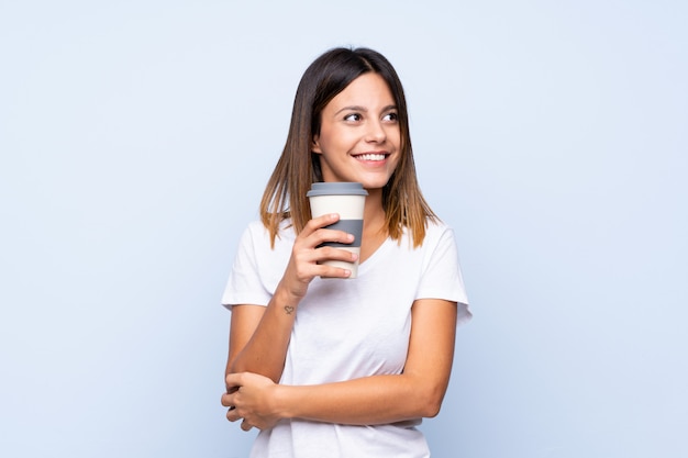 Junge Frau über dem lokalisierten blauen Hintergrund, der Kaffee hält, um wegzunehmen