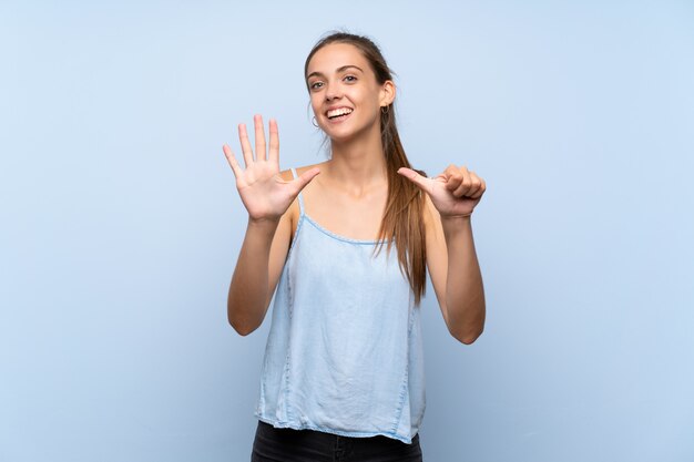 Junge frau über dem lokalisierten blauen hintergrund, der sechs mit den fingern zählt