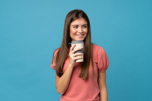 Junge Frau über der lokalisierten blauen Wand, die Kaffee hält, um wegzunehmen