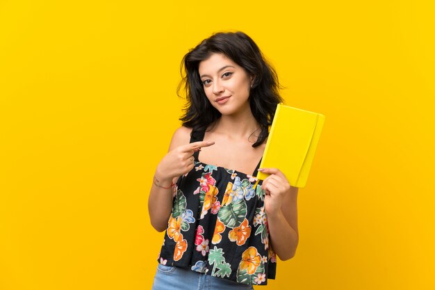 Junge Frau über der lokalisierten gelben Wand, die ein Buch hält und liest