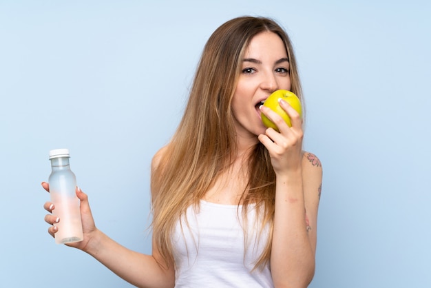 Junge Frau über getrenntem Blau mit einem Apfel und einer Flasche Wasser