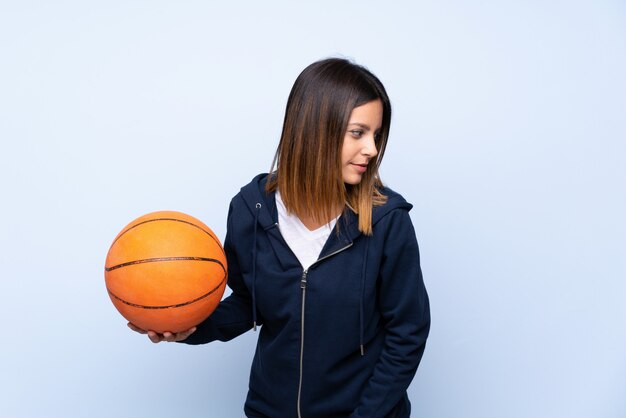 Junge Frau über getrenntem Blau mit Kugel des Basketballs