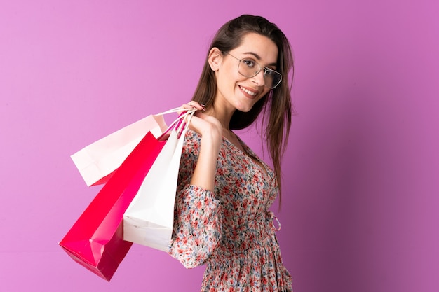 Junge Frau über isolierte lila Wand, die Einkaufstaschen hält und lächelt
