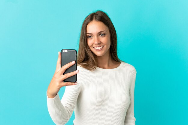 Junge Frau über isoliertem blauem Hintergrund macht ein Selfie