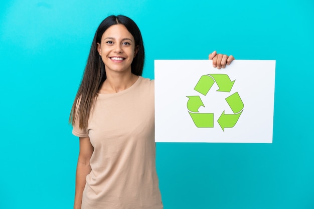Junge Frau über isoliertem Hintergrund, die ein Plakat mit Recycling-Symbol mit glücklichem Ausdruck hält