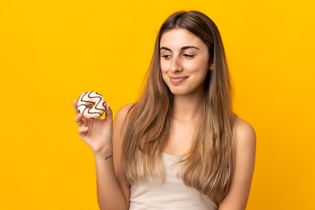 Junge Frau über isolierter gelber Wand, die einen Donut hält