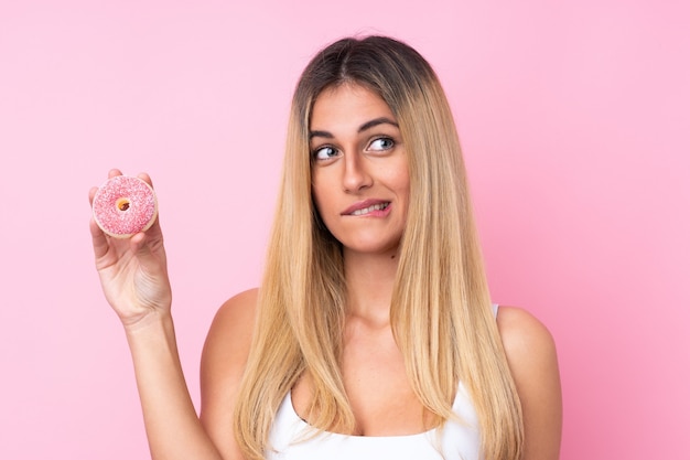 Junge Frau über isolierter rosa Wand, die einen Donut hält